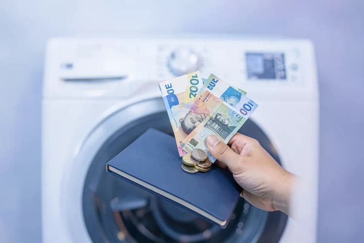 Uma mão segurando notas de dinheiro e moedas ao lado de um orçamento de conserto de máquina de lavar e secar.