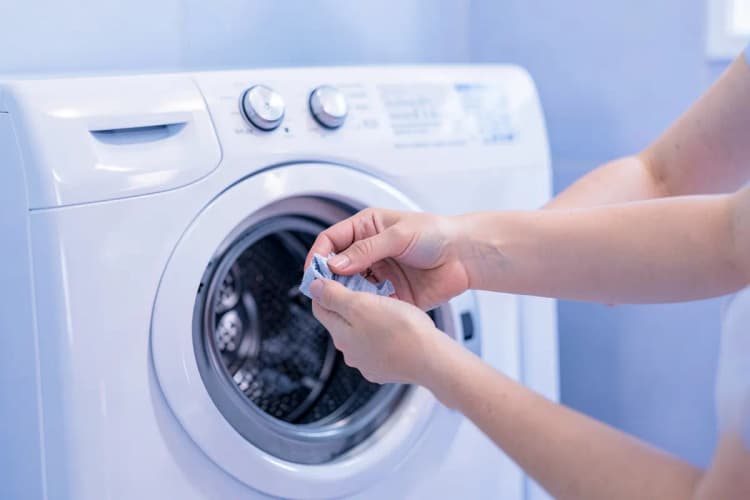 Mulher limpando o filtro de uma máquina de lavar e secar