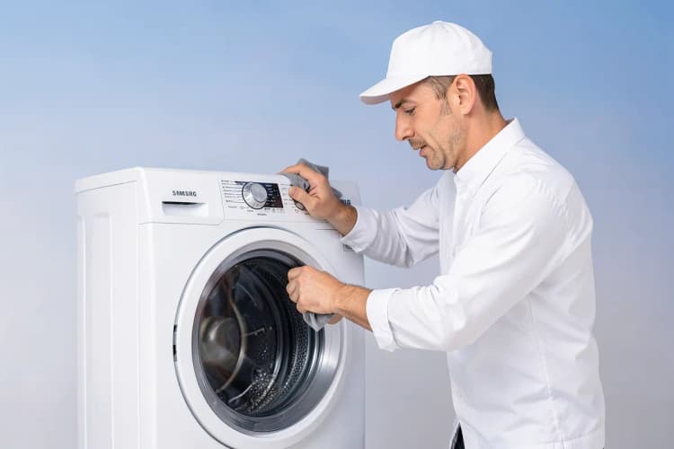 Homem de uniforme branco limpando a parte externa de uma máquina de lavar Samsung com um pano.
