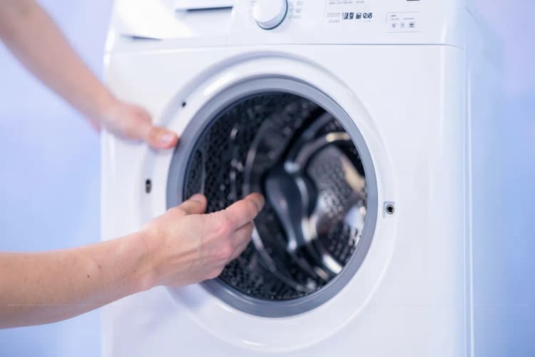 Uma pessoa examinando atentamente uma máquina de lavar e secar roupa em busca de problemas.