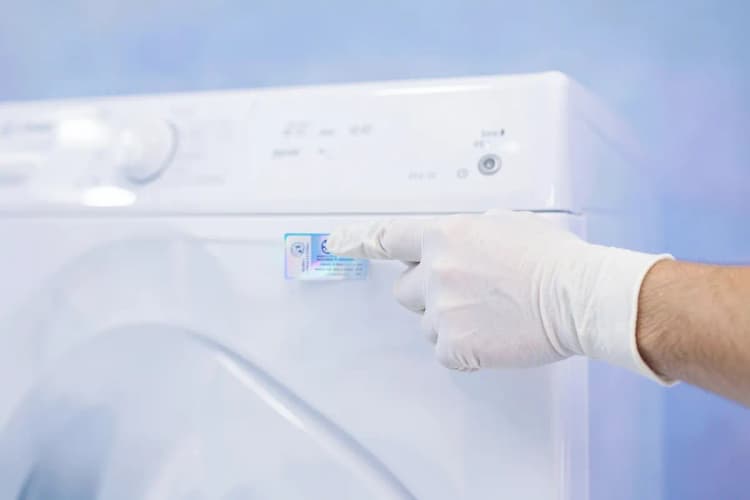Um técnico de serviço verificando a etiqueta de autorização em uma máquina de lavar e secar roupa.