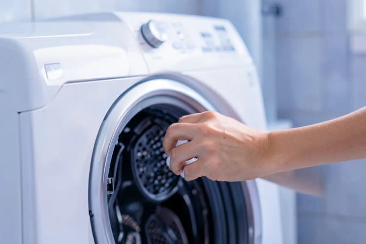 Mulher limpando o filtro de uma máquina de lavar roupa, plano detalhe, luz de banheiro, dia