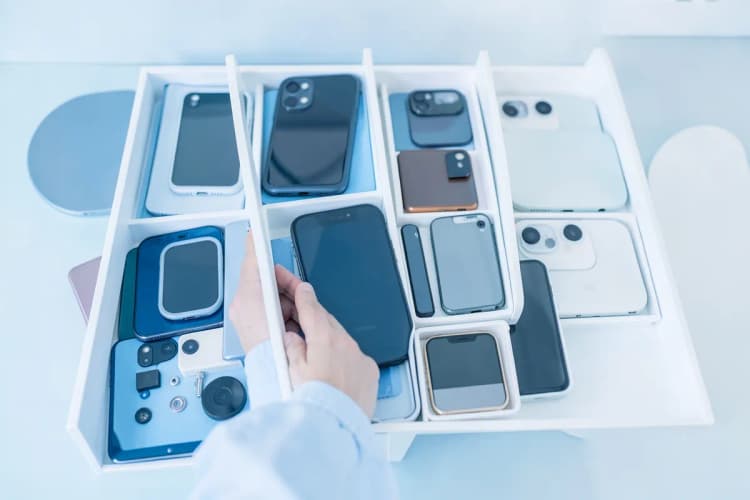 Um técnico de celular mostrando uma variedade de peças de reposição, como telas, baterias e câmeras, organizadas em compartimentos.