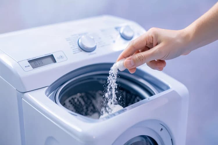 Mão colocando sabão em pó no dispenser de uma lava e seca, com foco no compartimento.