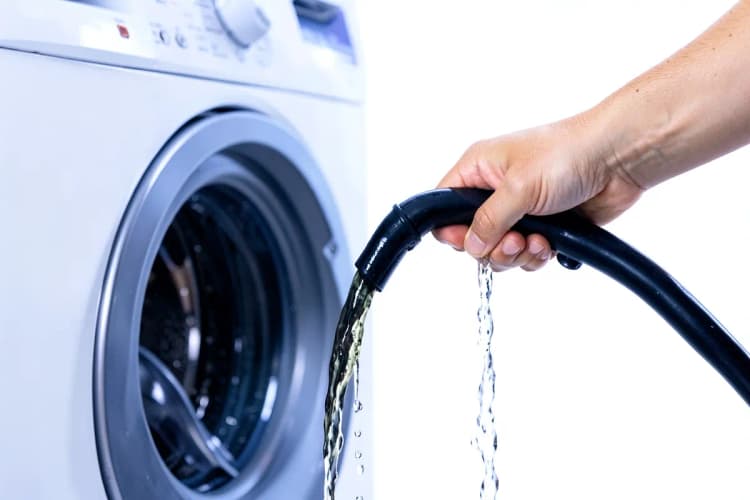 Mão segurando uma mangueira de drenagem de máquina de lavar com água escura saindo.