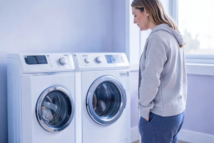 Pessoa pensativa olhando para uma máquina de lavar e secar roupa antiga.