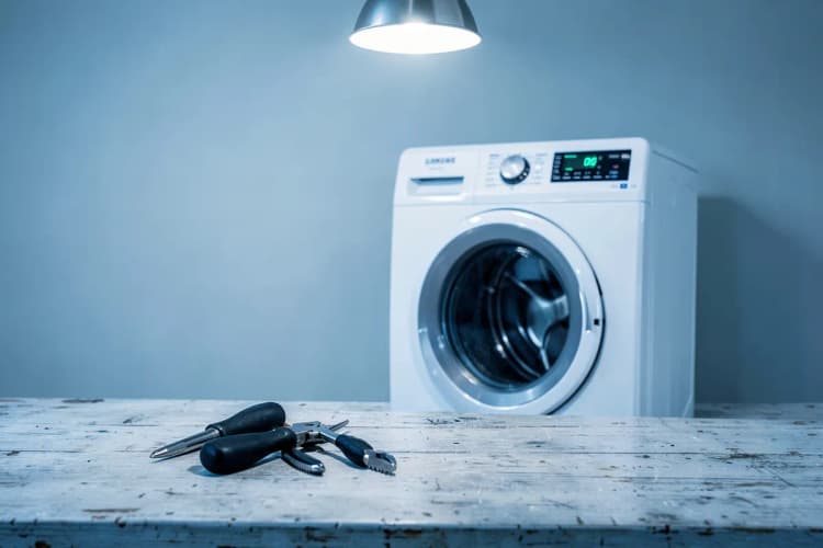 Ferramentas como chave de fenda e alicate dispostas sobre uma bancada perto de uma máquina de lavar Samsung.