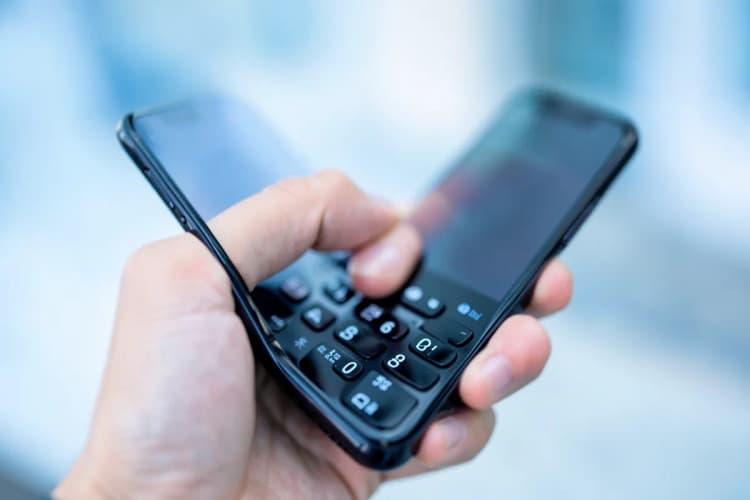 Mão segurando um telefone e discando um número em um teclado numérico.