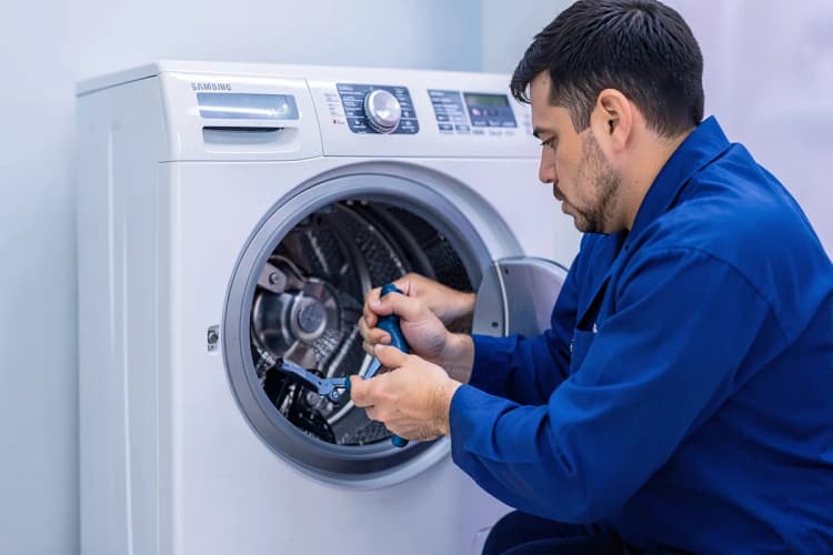 Um técnico de uniforme azul trabalhando no interior de uma máquina lava e seca Samsung aberta.