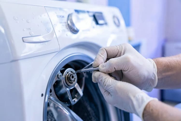 Close-up de um técnico de serviço trabalhando em uma máquina de lavar e secar roupa com ferramentas