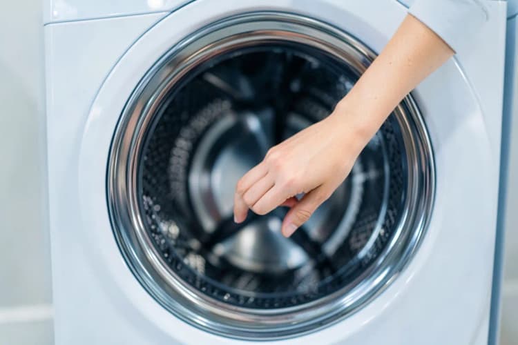 Mão humana verificando o interior de um tambor de máquina de lavar e secar, procurando por objetos estranhos.