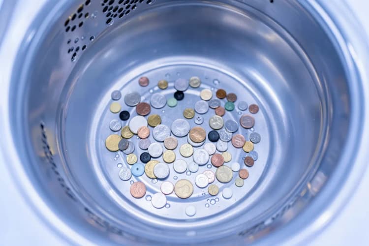 Pequenos objetos como moedas e botões espalhados no fundo do tambor de uma máquina de lavar e secar.