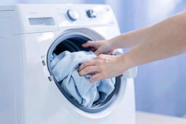 Pessoa colocando roupas em uma máquina de lavar e secar.