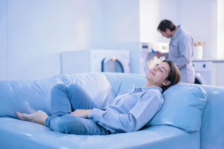 Pessoa relaxando em um sofá enquanto um profissional realiza um serviço em segundo plano.