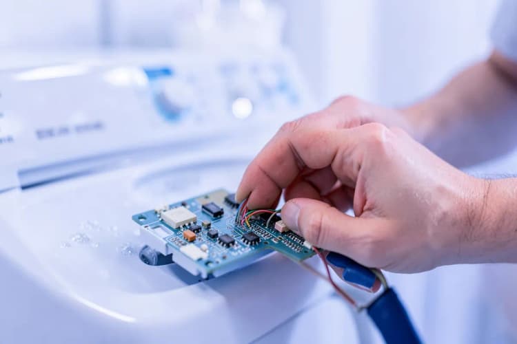 Mãos de técnico consertando placa de circuito de lava e seca, em close-up.