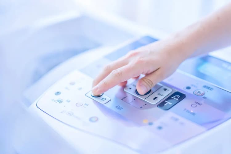 Uma mão humana pressionando botões em um painel de controle de máquina de lavar.