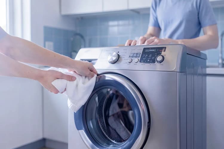 Uma pessoa organizando roupas limpas ao lado de uma máquina lava e seca.