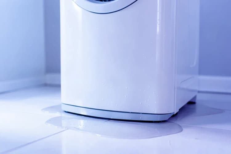 Close-up de uma máquina de lavar e secar com água vazando no chão.