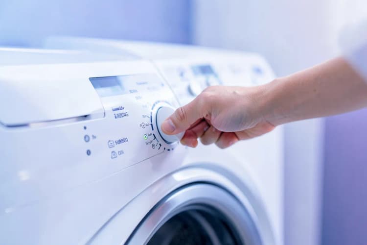 Uma mão girando um botão de controle em uma máquina de lavar e secar roupa.